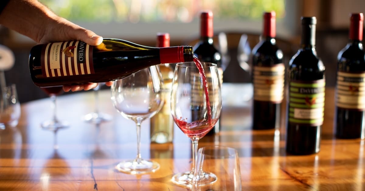 Person pouring DaVero wine into a glass at a wine tasting table with bottles and glasses.