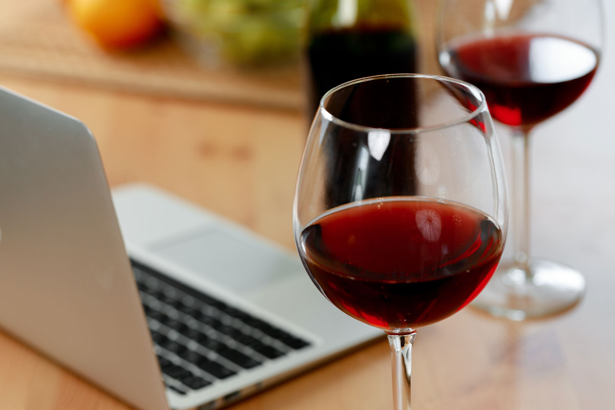 glass of wine with laptop in use next to it